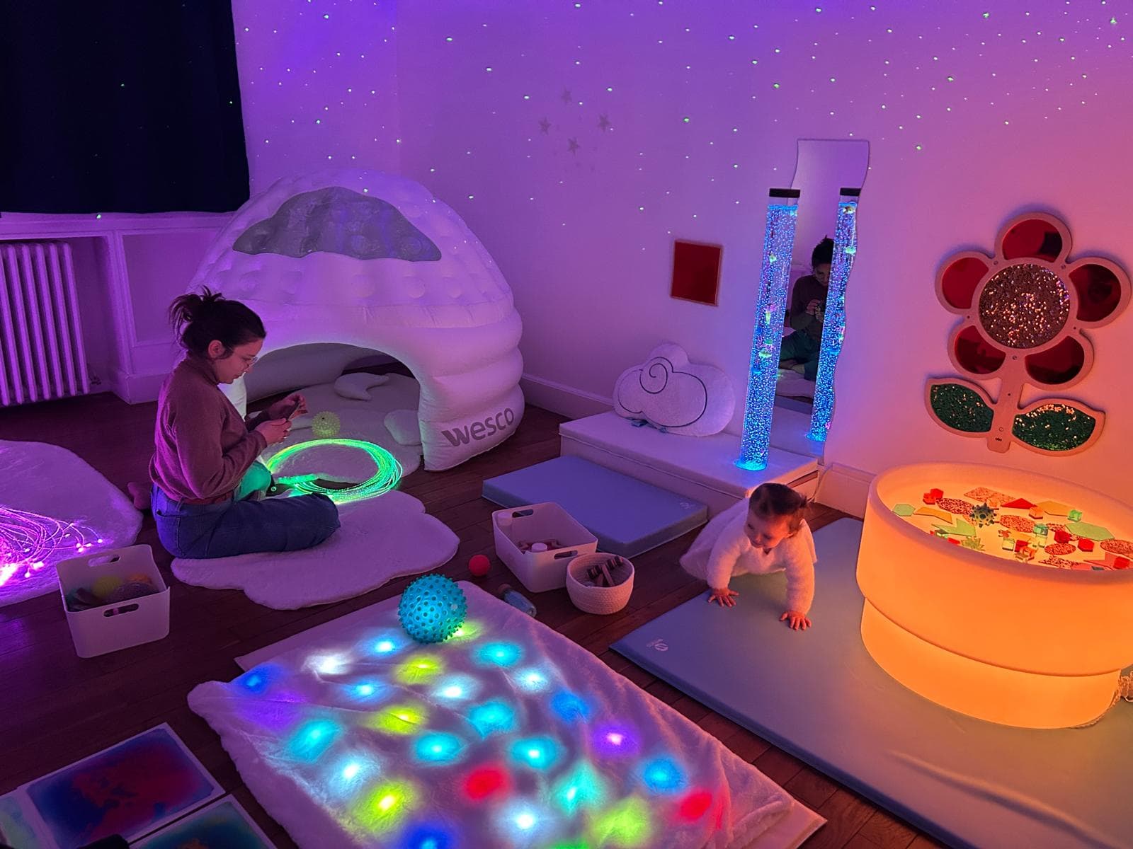 Salle Snoezelen avec maman et enfant explorant les fibres optiques et colonnes à bulles