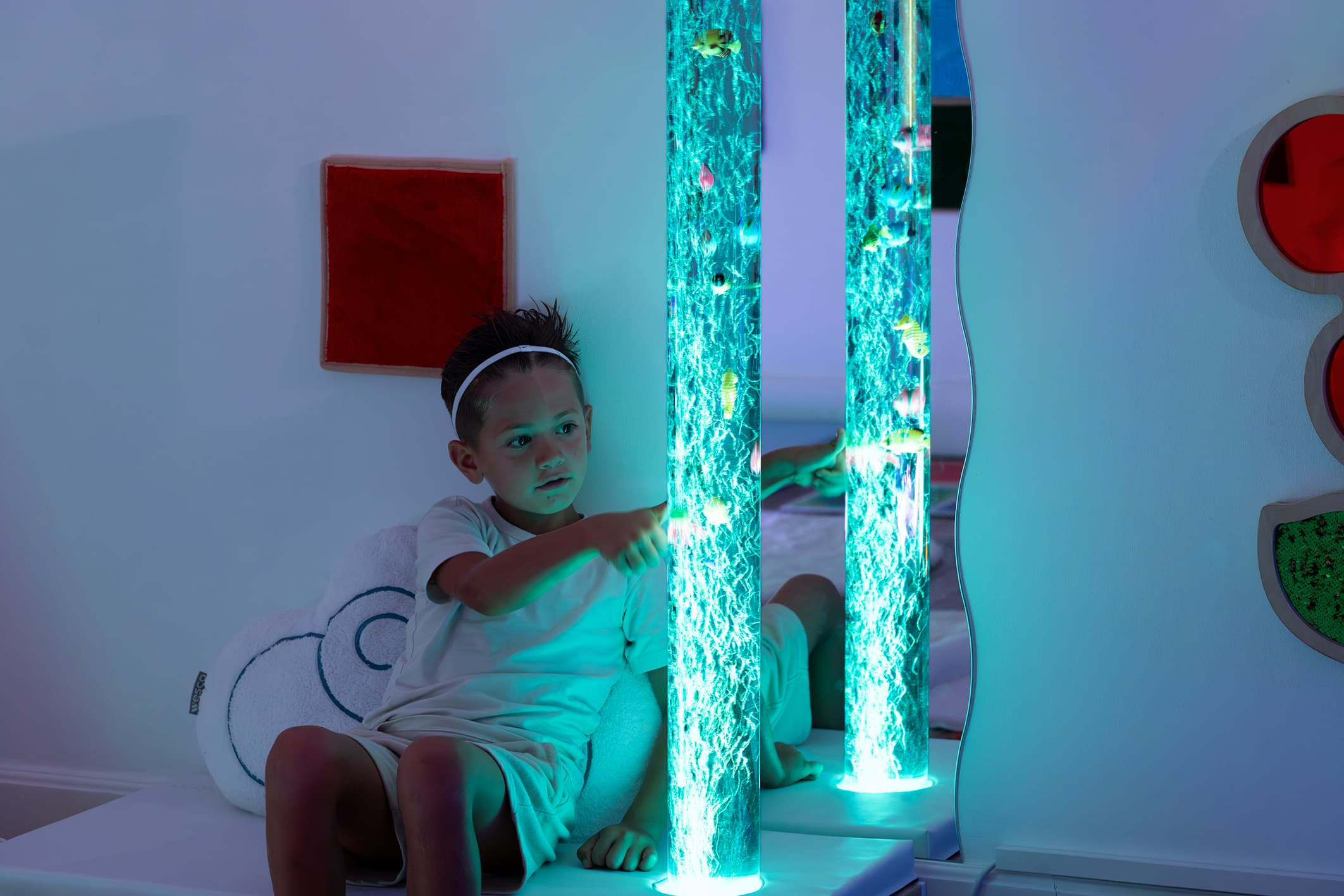 Enfant explorant une colonne à bulles lumineuse dans un espace Snoezelen